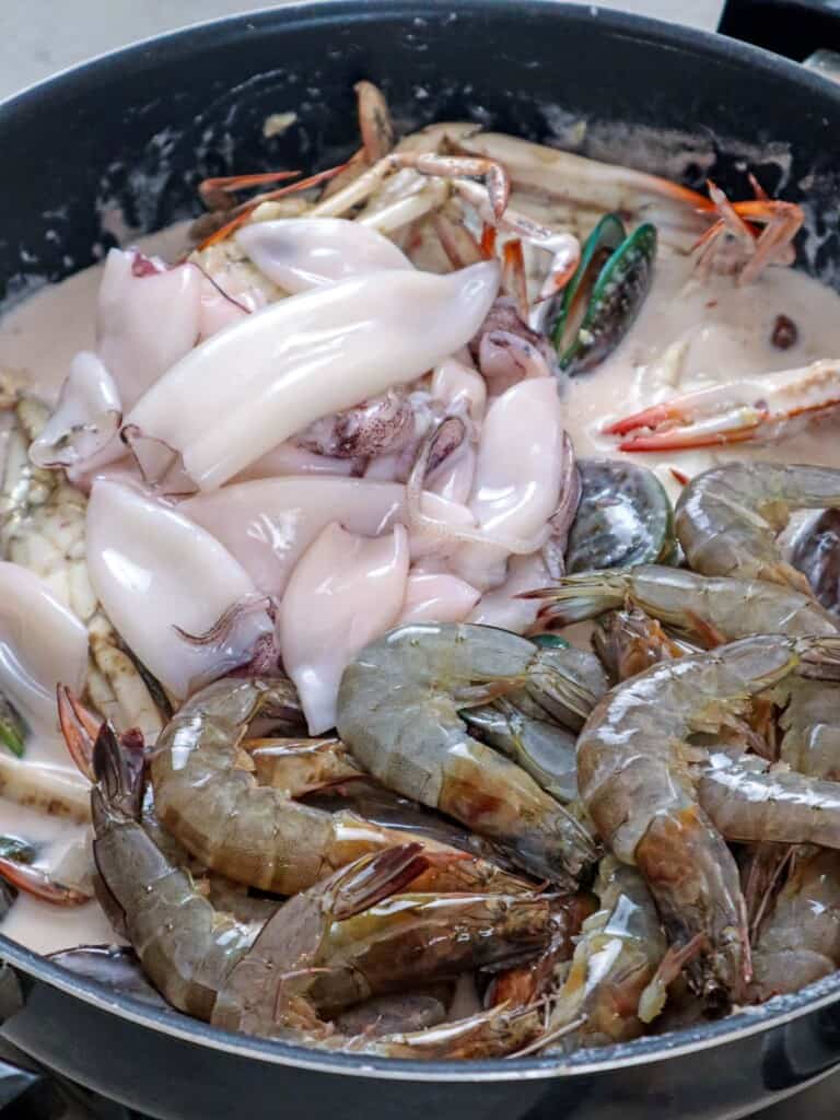 cooking shrimp, squid, crab, and mussels in a coconut sauce in a wide pan