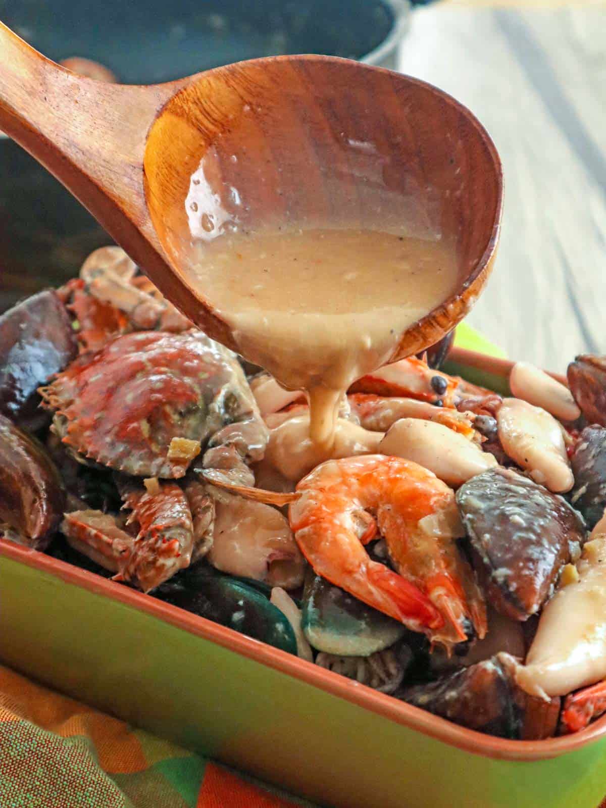 pouring coconut sauce over ginataang seafood in serving dish