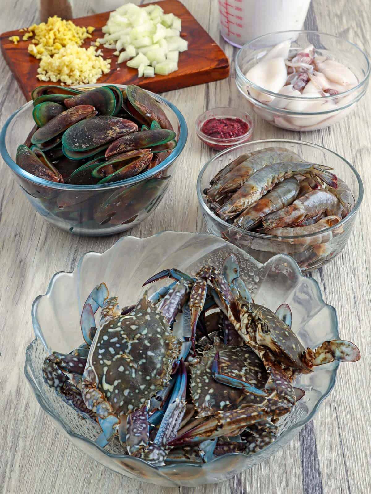 uncooked crab, shrimp, mussels, squid, minced garlic, chopped onions, shrimp paste in bowls