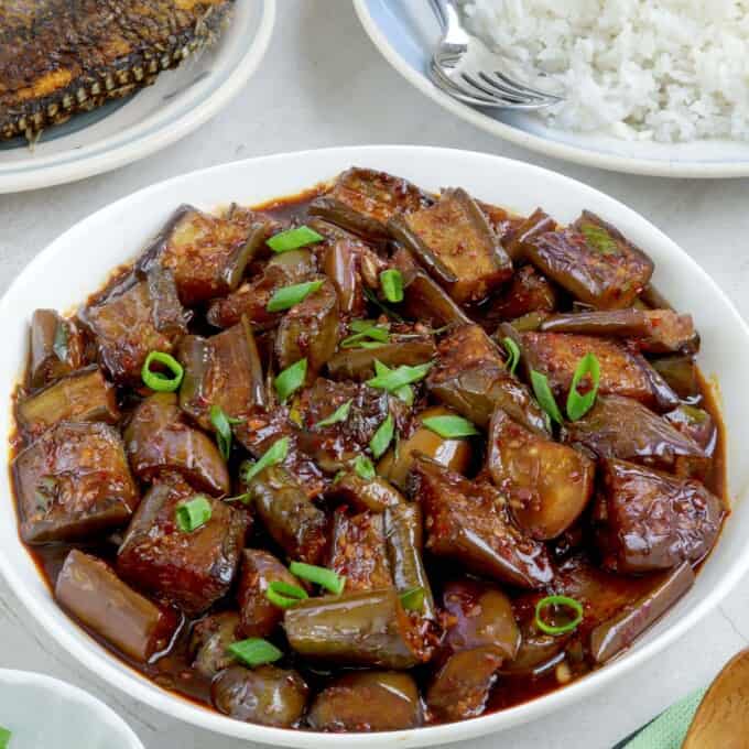 talong stir-fry in a white bowl with steamed rice and fried fish on the side