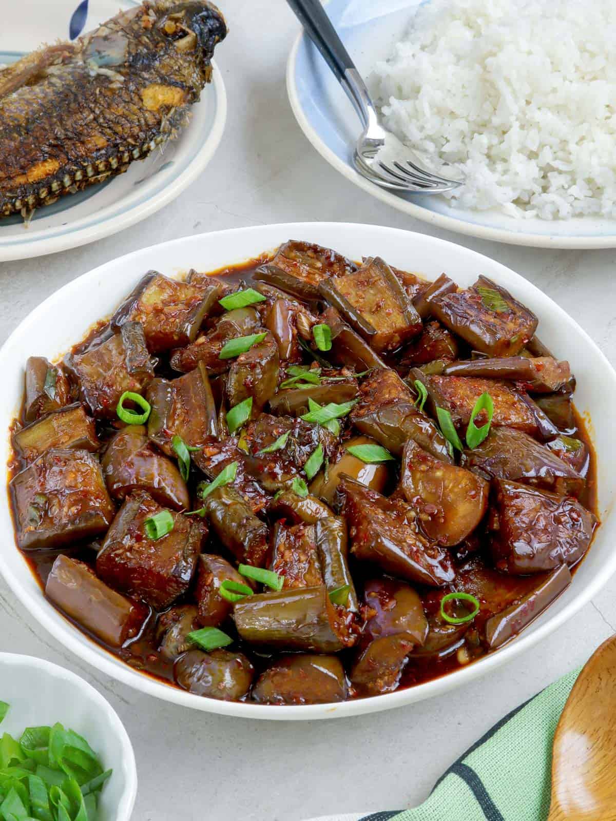 talong stir-fry in a white bowl with steamed rice and fried fish on the side