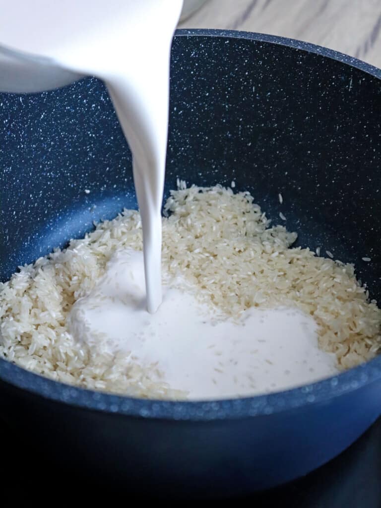 pouring coconut milk over rice in a pot