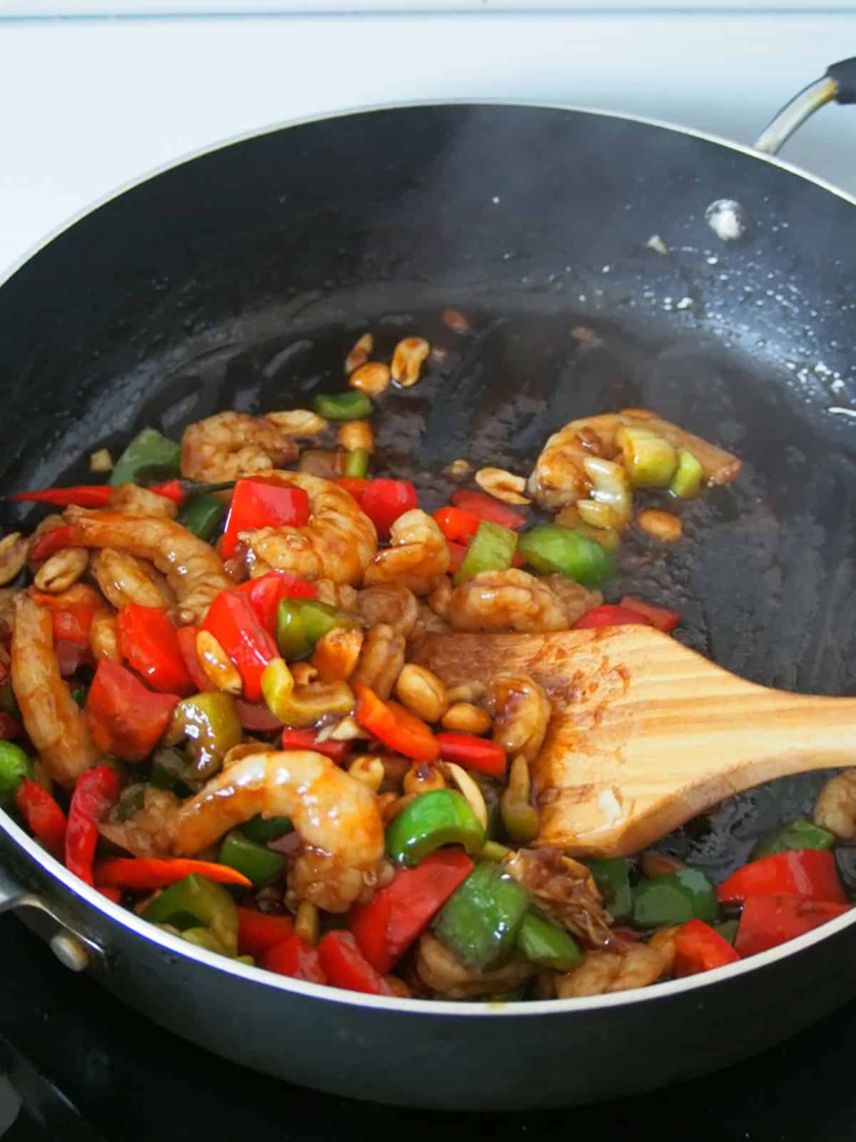 stir-frying shrimp in a wide pan with peanuts, bell peppers, and celery