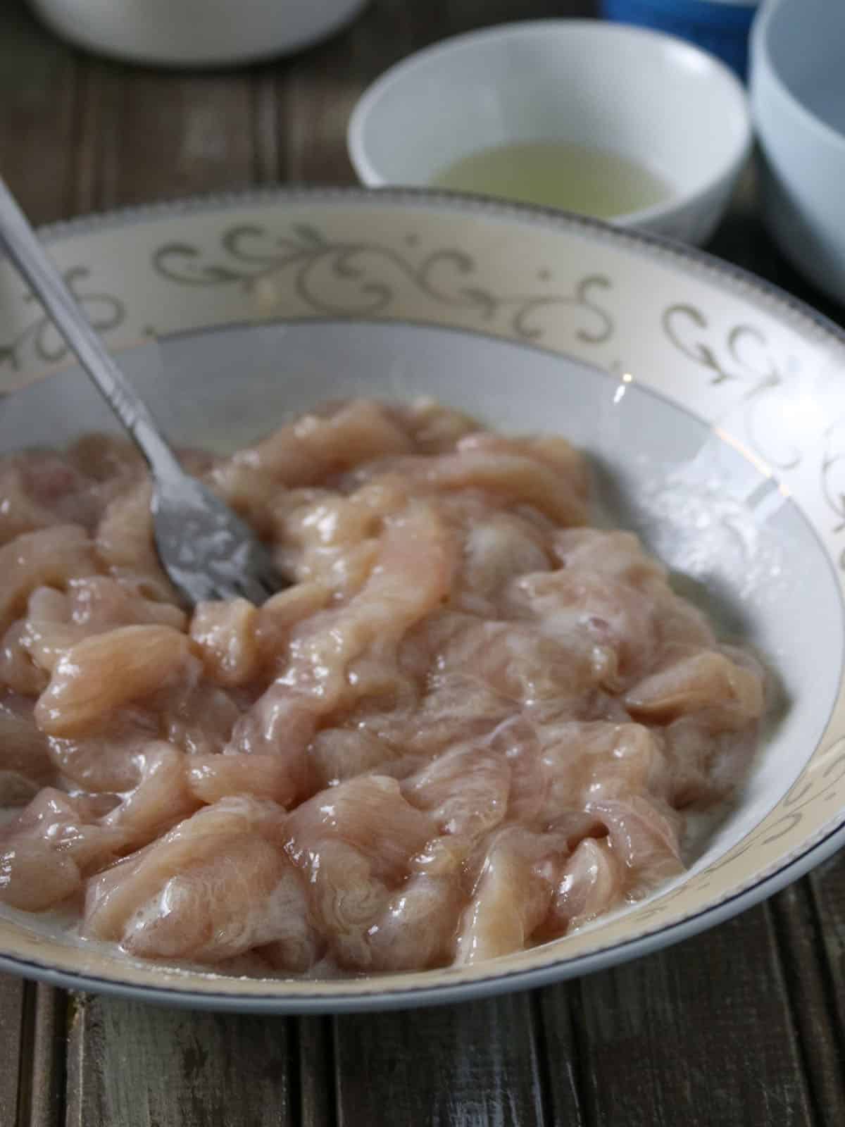 velveting sliced chicken breast in a bowl