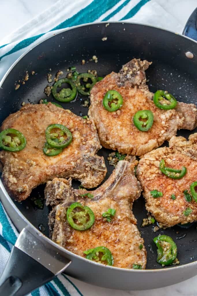salt and pepper pork chops with sliced jalapenos and browned garlic in a wide pan