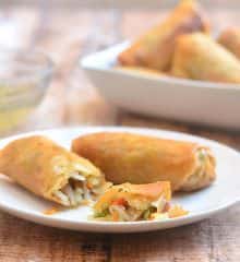Lumpiang Prito with Pork om a white serving plate with a bowl of spicy vinegar on the side