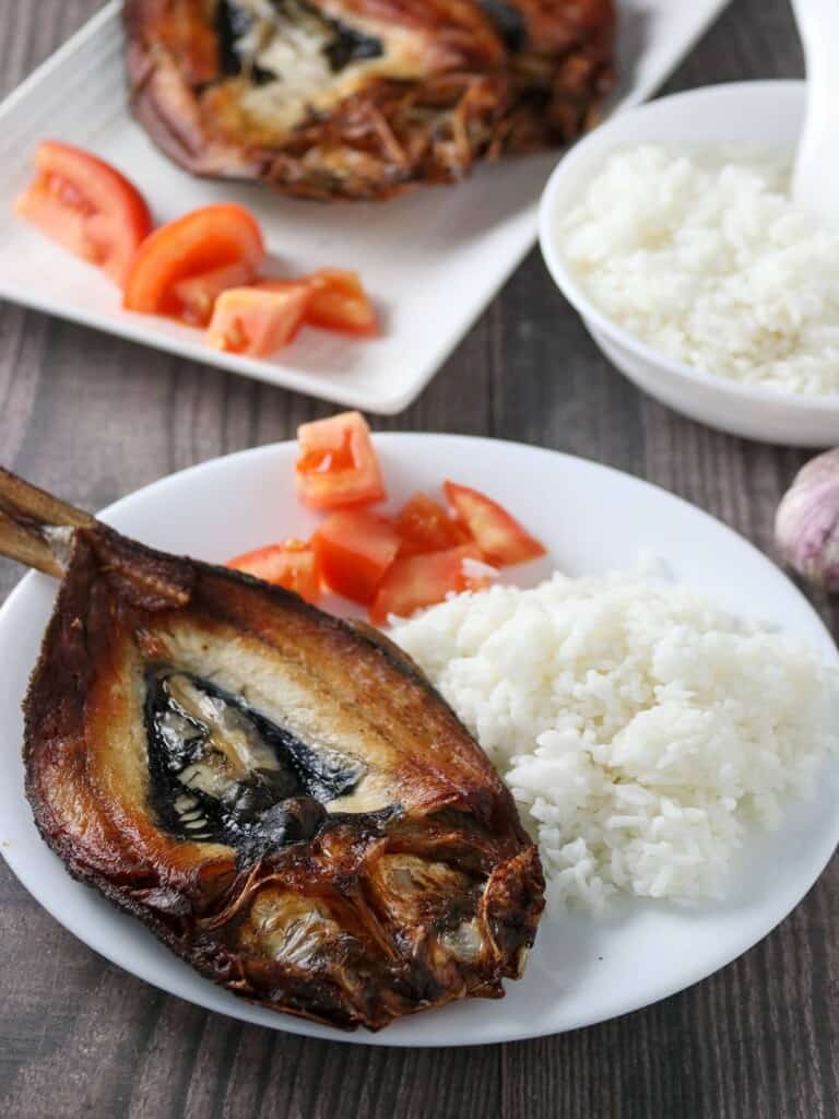 fried butterflied milkfish on a white plate with steamed rice and chopped tomatoes