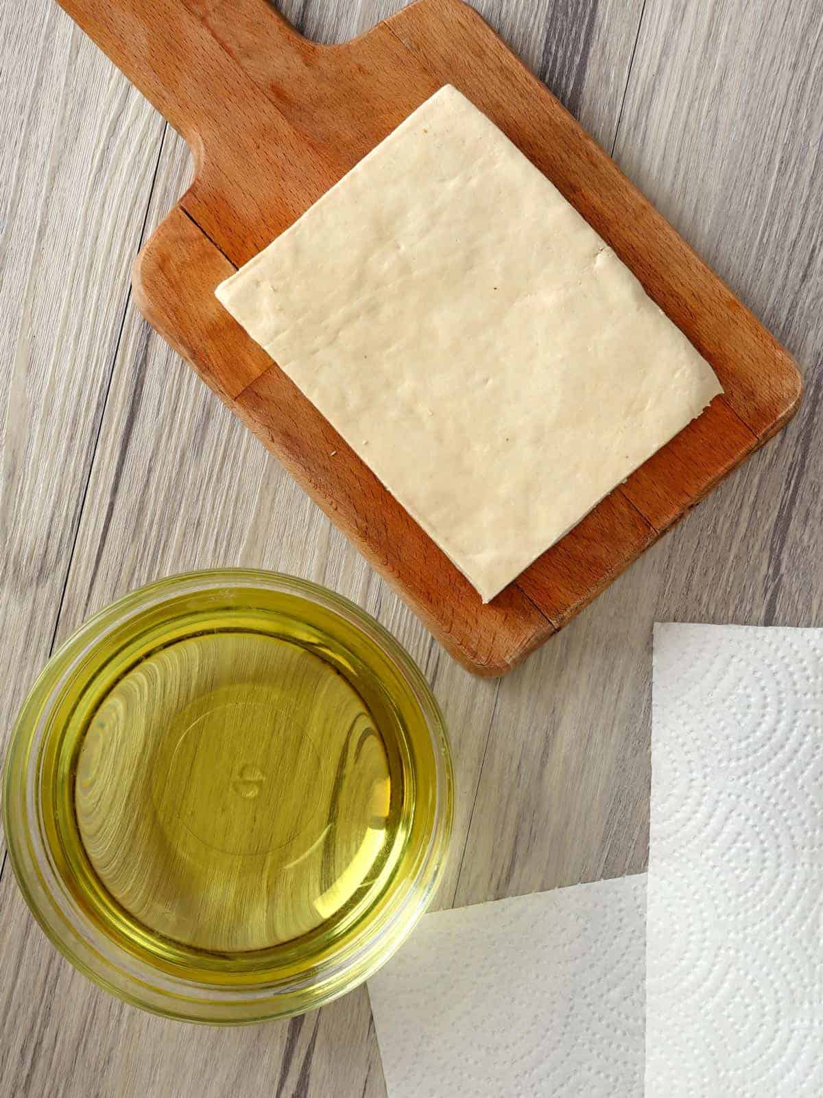 firm tofu block on a cutting board and a bowl of oil