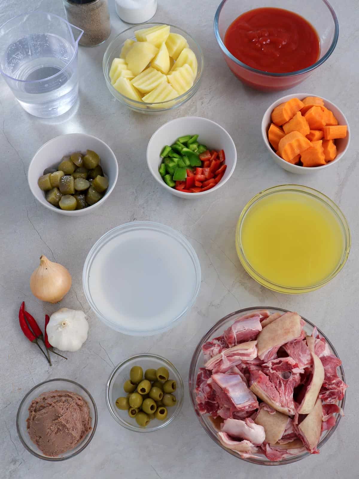 goat meat, vinegar, pineapple juice, gherkins, green olives, bell peppers, tomato sauce, cheese, carrots, potatoes, tomato sauce, liver spread in bowls