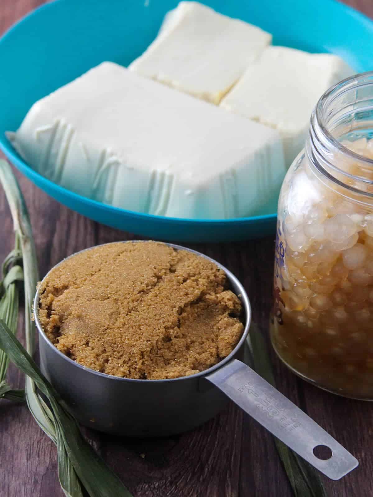 brown sugar in a scoop, cooked sago pearls in a glass jar, silken tofu in a blue bowl