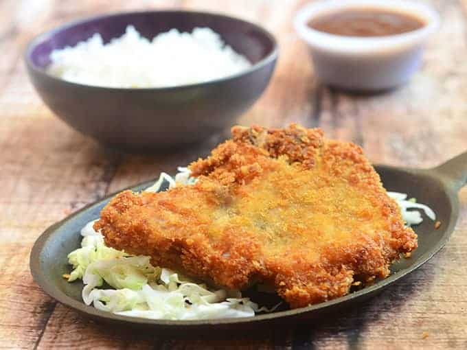 This crispy pork chop is served over a bed of cabbage with rice on the side.