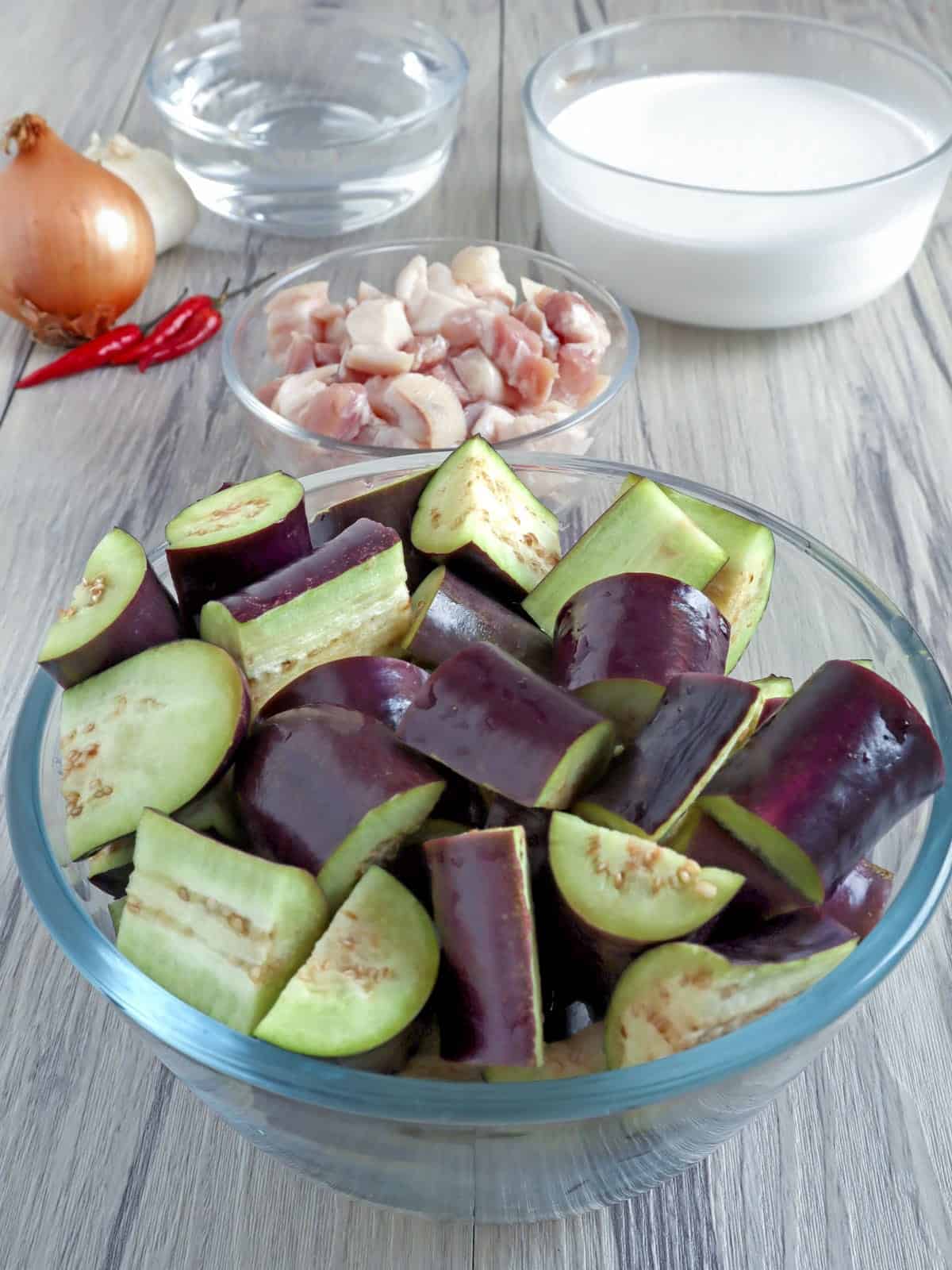 cubed eggplants, diced pork belly, coconut milk in individual bowls with chili pepper and brown onion on the side