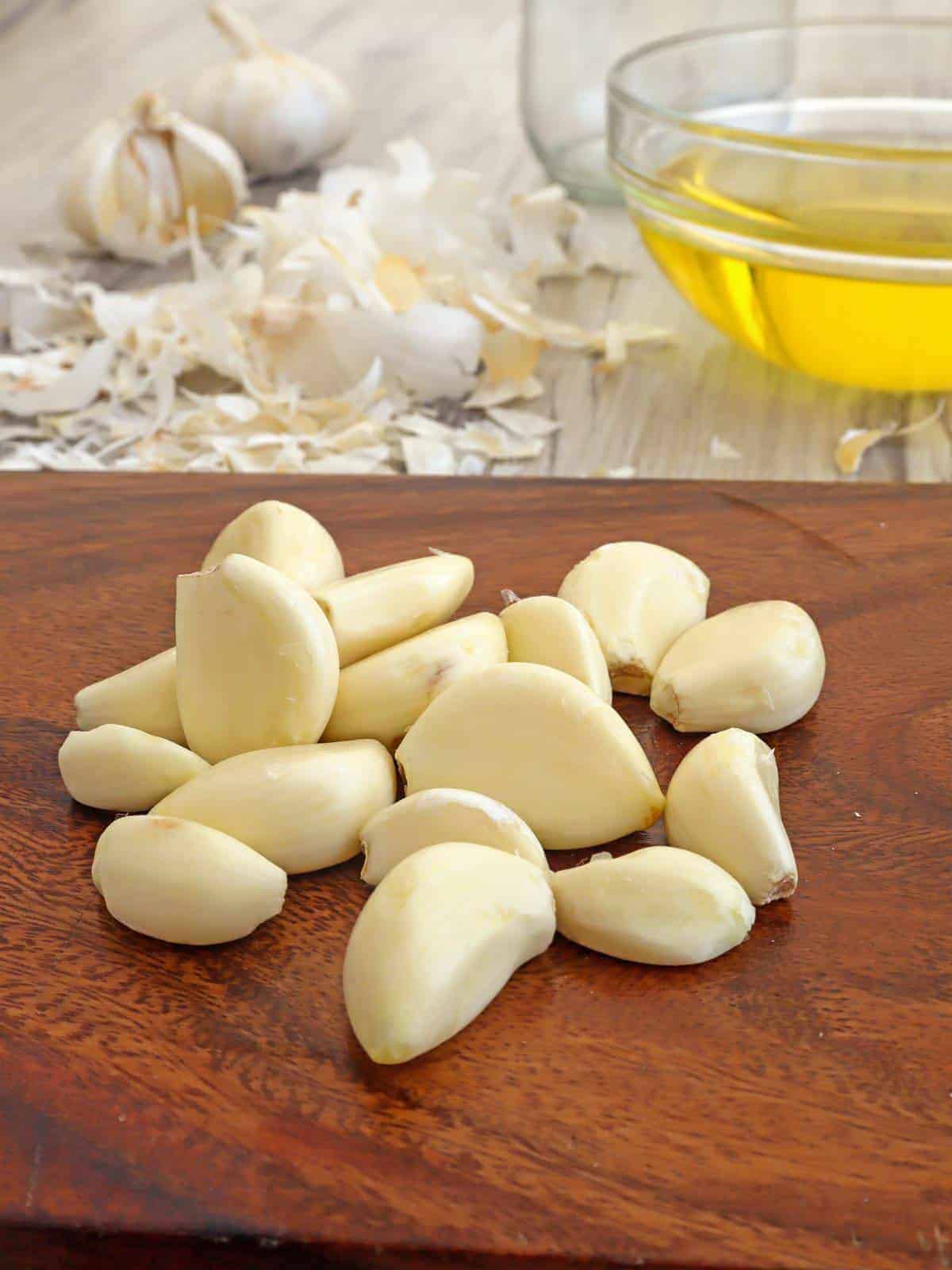 peeled garlic on a cutting board and a bowl of canola oil on the side