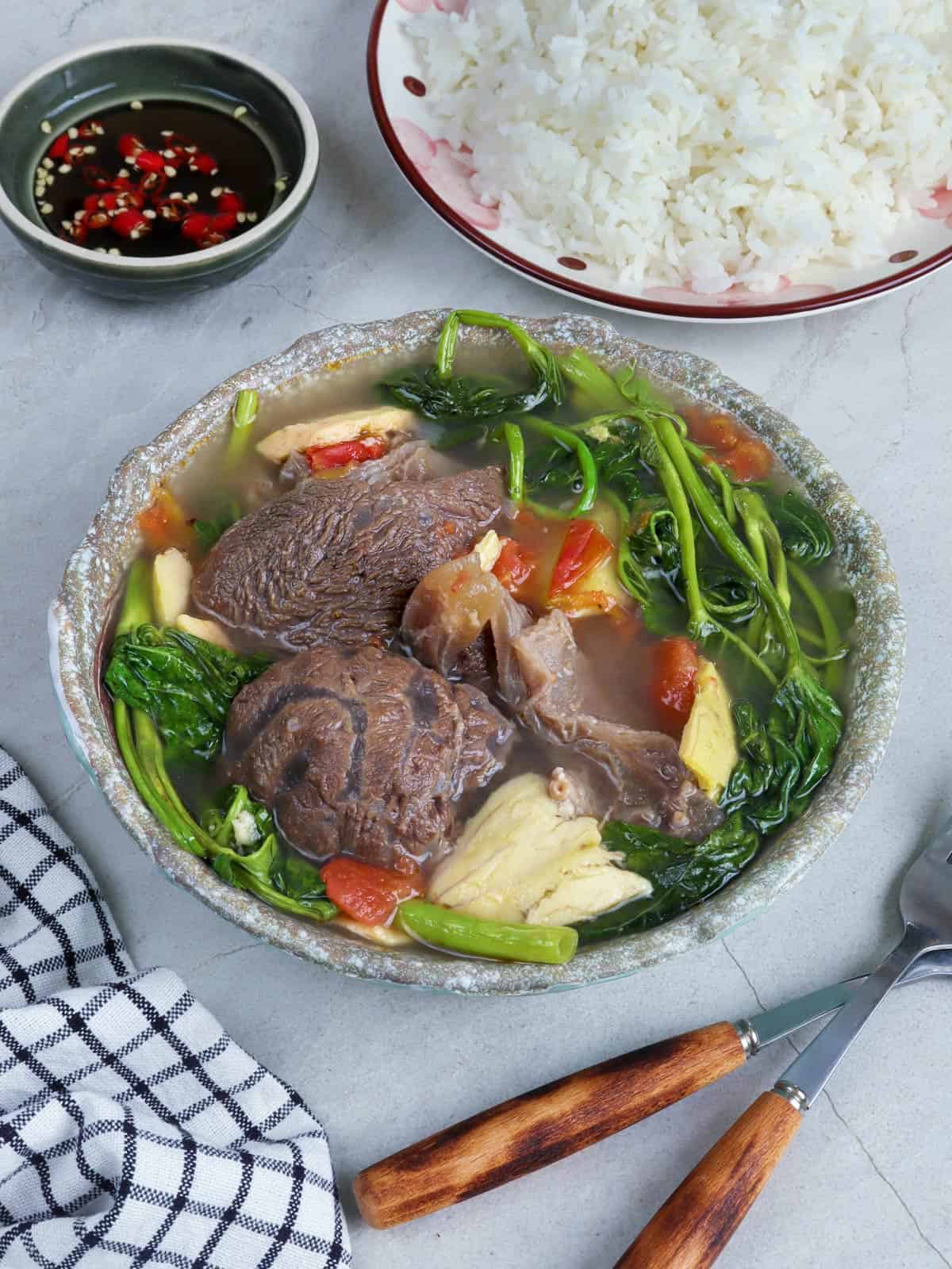 Sinigang na Baka sa Bayabas in a serving bowl with a plate of steamed rice and a dish of patis on the side