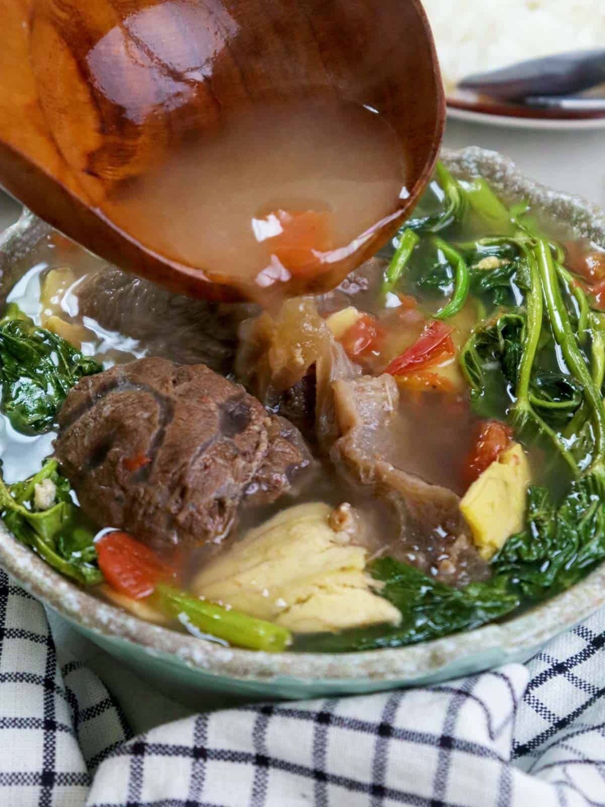 pouring broth on a bowl of beef sinigang with guavas