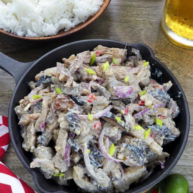 Dinakdakan in a cast iron skillet with a bowl of steamed rice on the side and a glass of beer