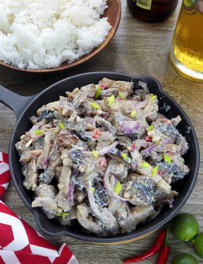 Dinakdakan in a cast iron skillet with a bowl of steamed rice on the side and a glass of beer