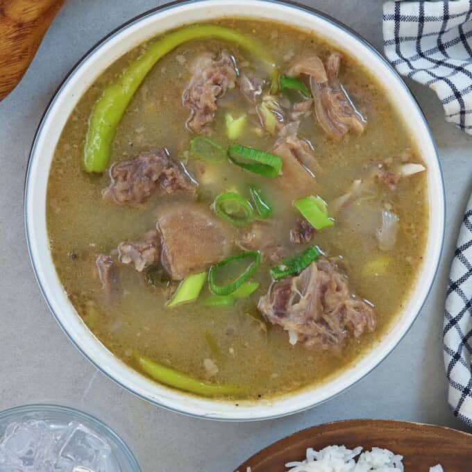 Sinampalukang Kambing in a white serving bowl with a plate of steamed rice on the side