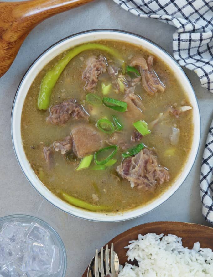 Sinampalukang Kambing in a white serving bowl with a plate of steamed rice on the side