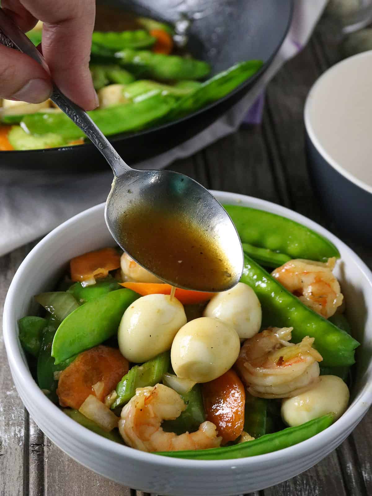 spooning sauce on vegetable stir fry in a white bowl