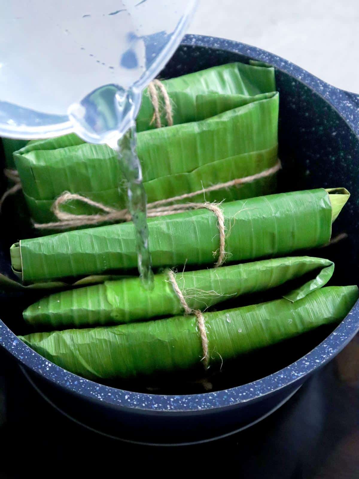 pouring water to banana-wrapped fish in a pot