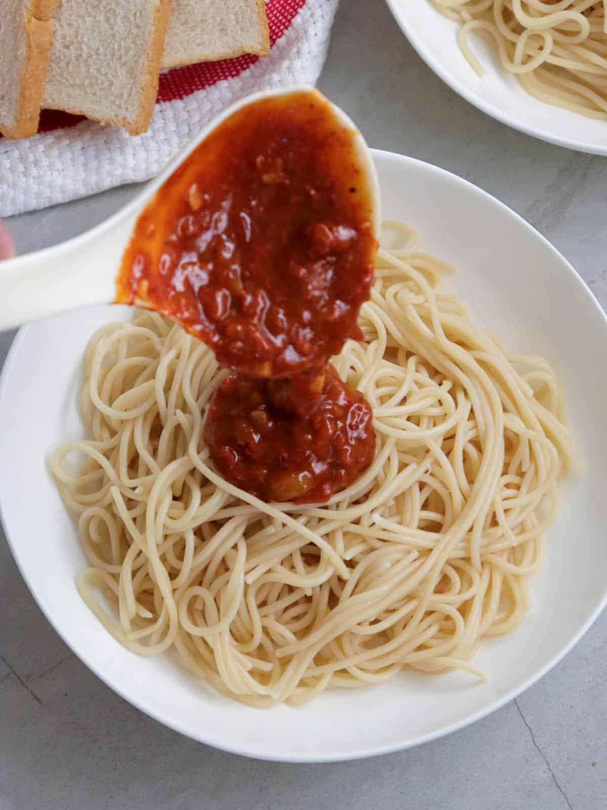 ladling meat sauce on a plate of spaghetti
