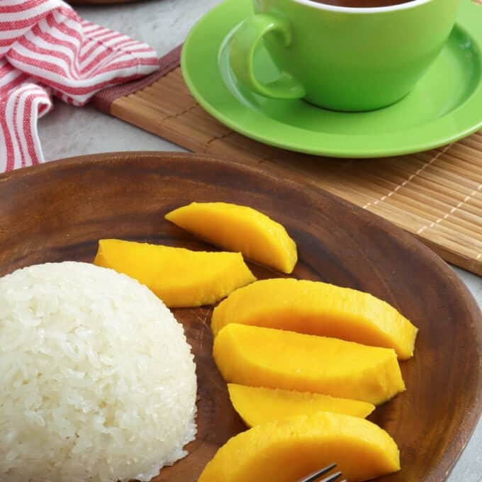 puto maya, sliced mangoes on a wooden plate with a cup of hot chocolate on the side