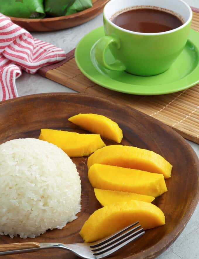 puto maya, sliced mangoes on a wooden plate with a cup of hot chocolate on the side