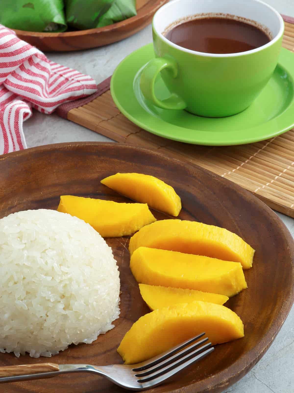 puto maya, sliced mangoes on a wooden plate with a cup of hot chocolate on the side