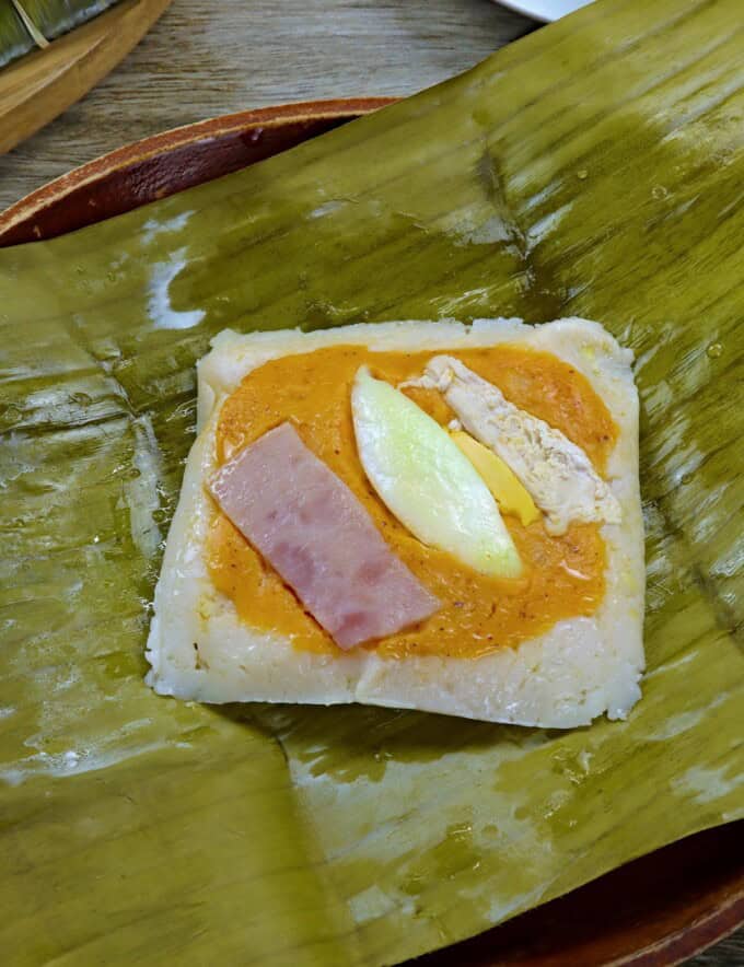 filipino tamales topped with flaked chicken and and hard boiled eggs on a serving plate.