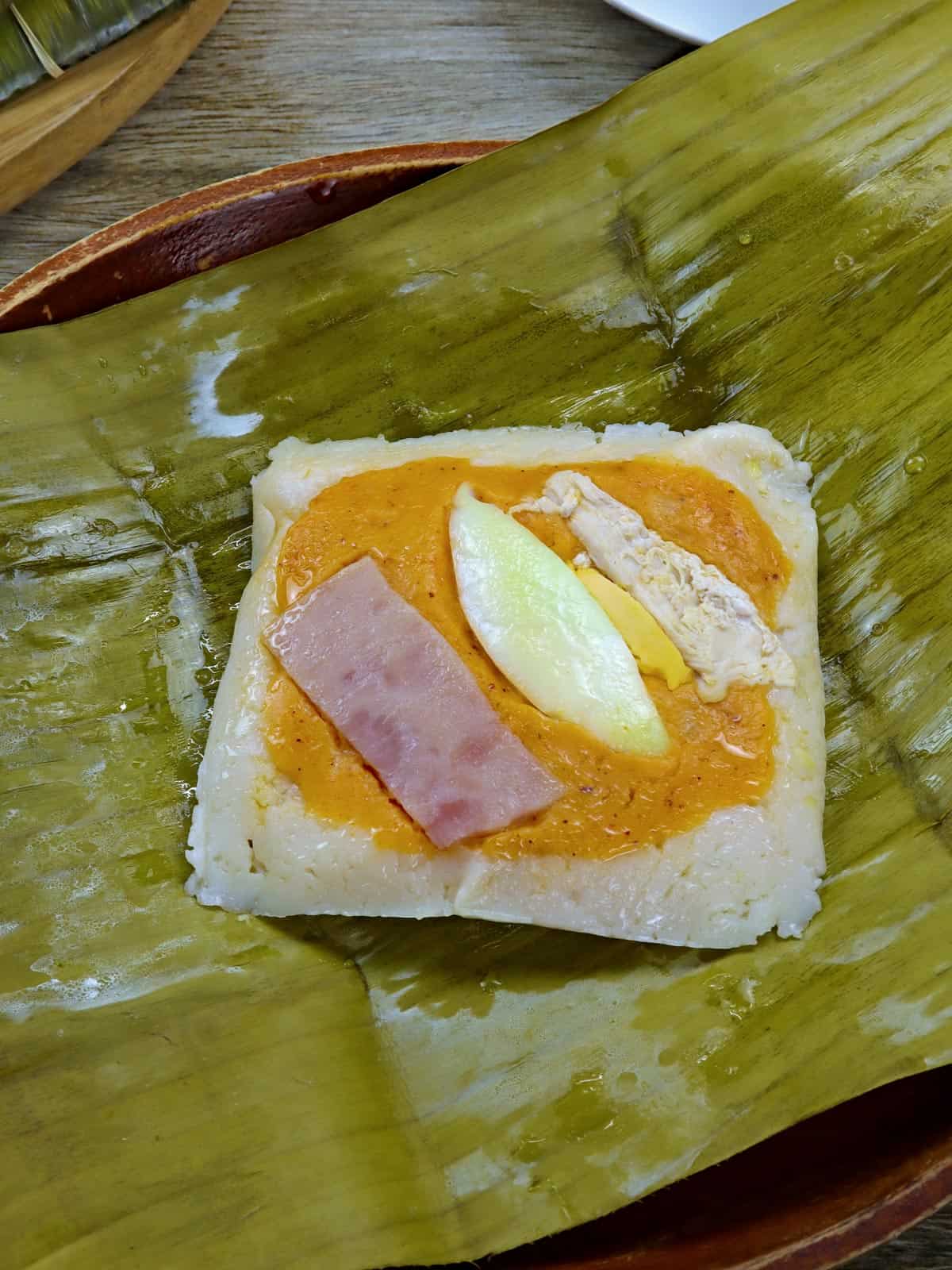 filipino tamales topped with flaked chicken and and hard boiled eggs on a serving plate.