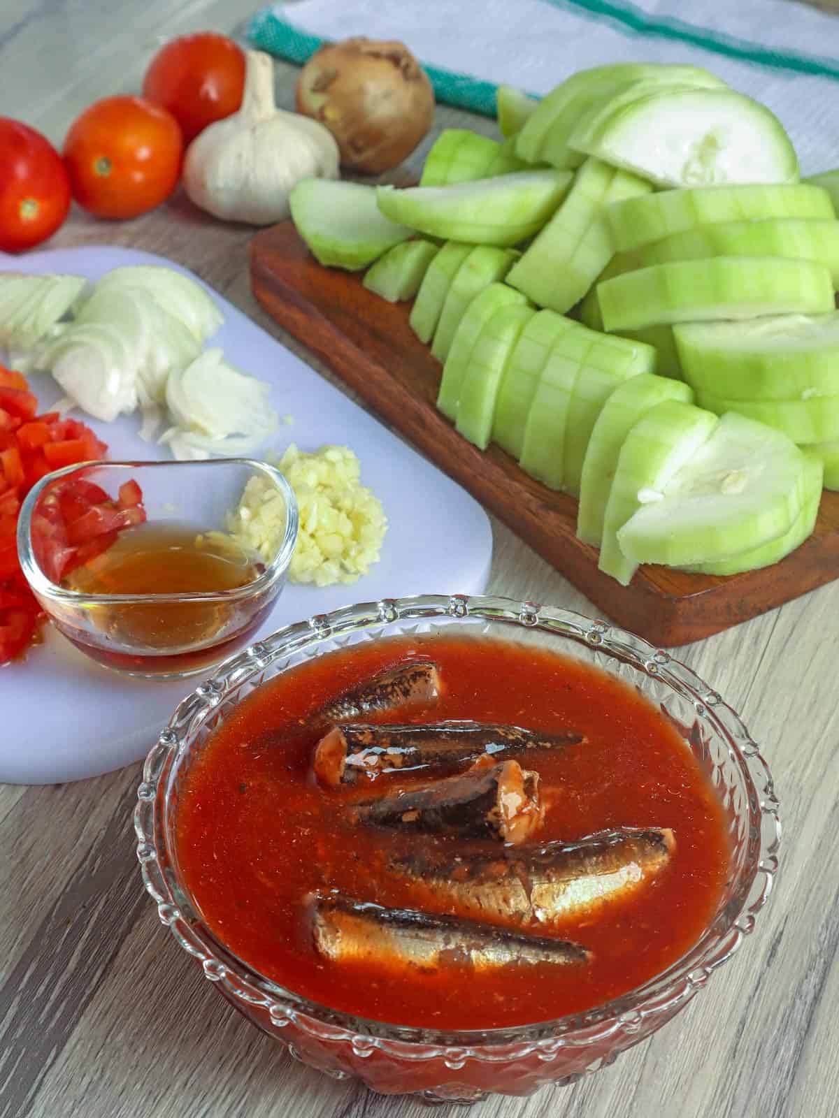 bowl with sardines in tomatoes, chopped onions, tomatoes, garlic, and sliced upo