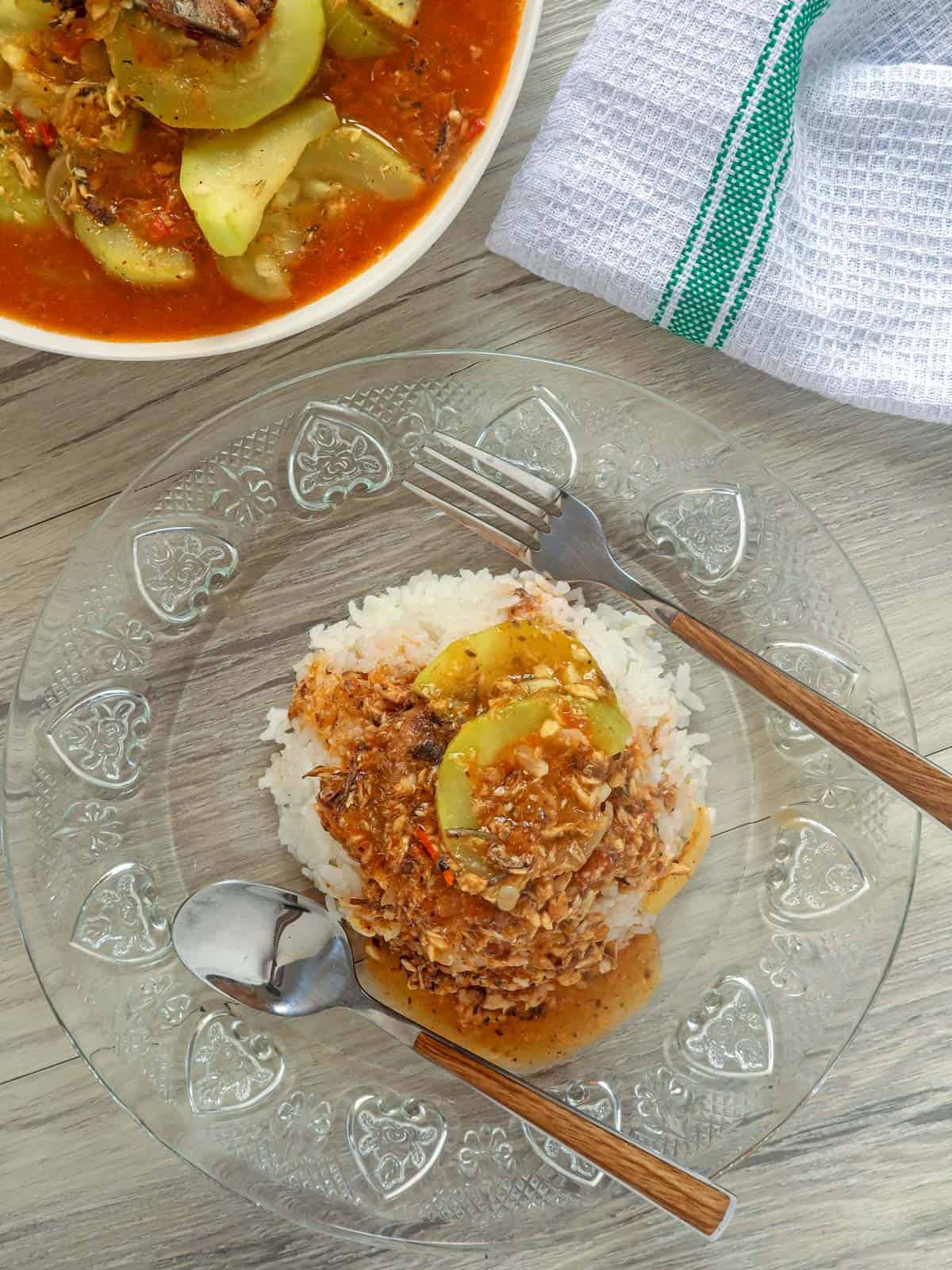 ginisang upo at sardinas over steamed rice on a clear, glass plate