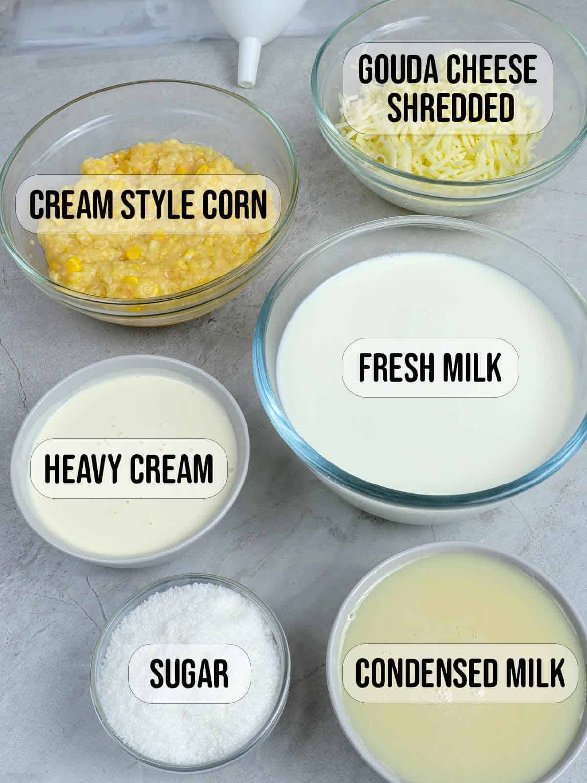 cream style corn, condensed milk, heavy cream, sugar, shredded cheese, whole milk in bowls.