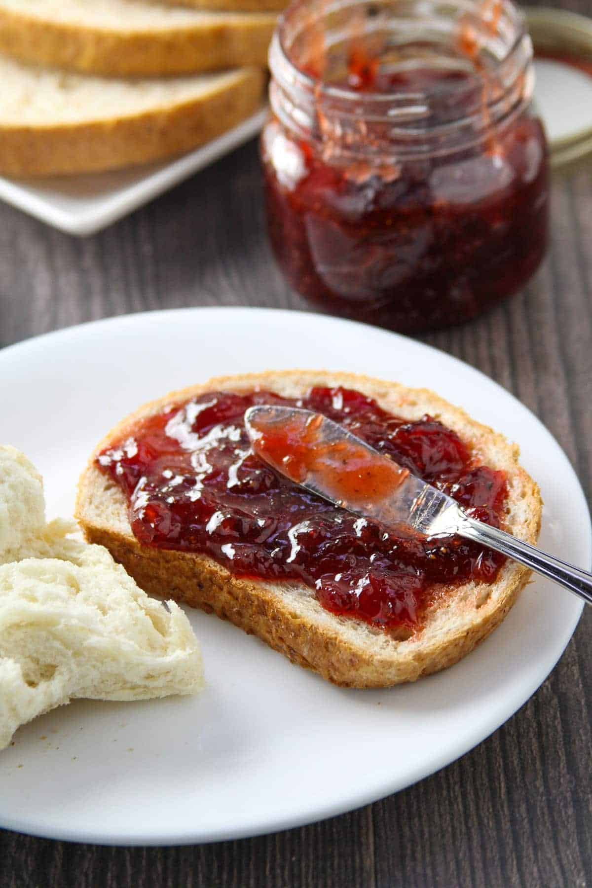 wheat toast with black pepper strawberry jam on a white plate with a jar of jam on the side