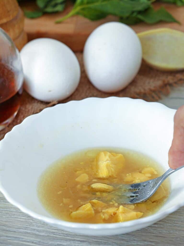mashing hard boiled egg yolk in broth with a fork