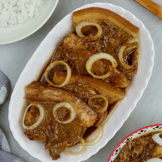 pork bistek garnished with onion rings on a serving platter with a plate of steamed rice on the side