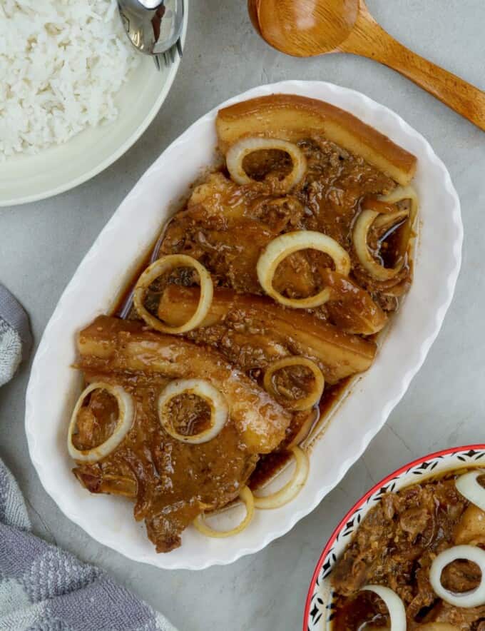 pork bistek garnished with onion rings on a serving platter with a plate of steamed rice on the side