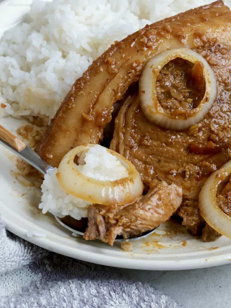 Filipino-style pork steak over rice on a white plate