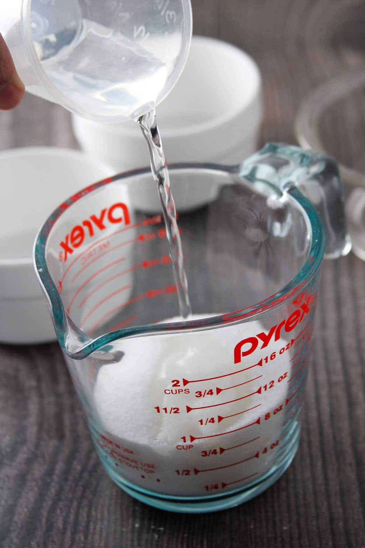 pouring water to sugar in a glass measuring cup