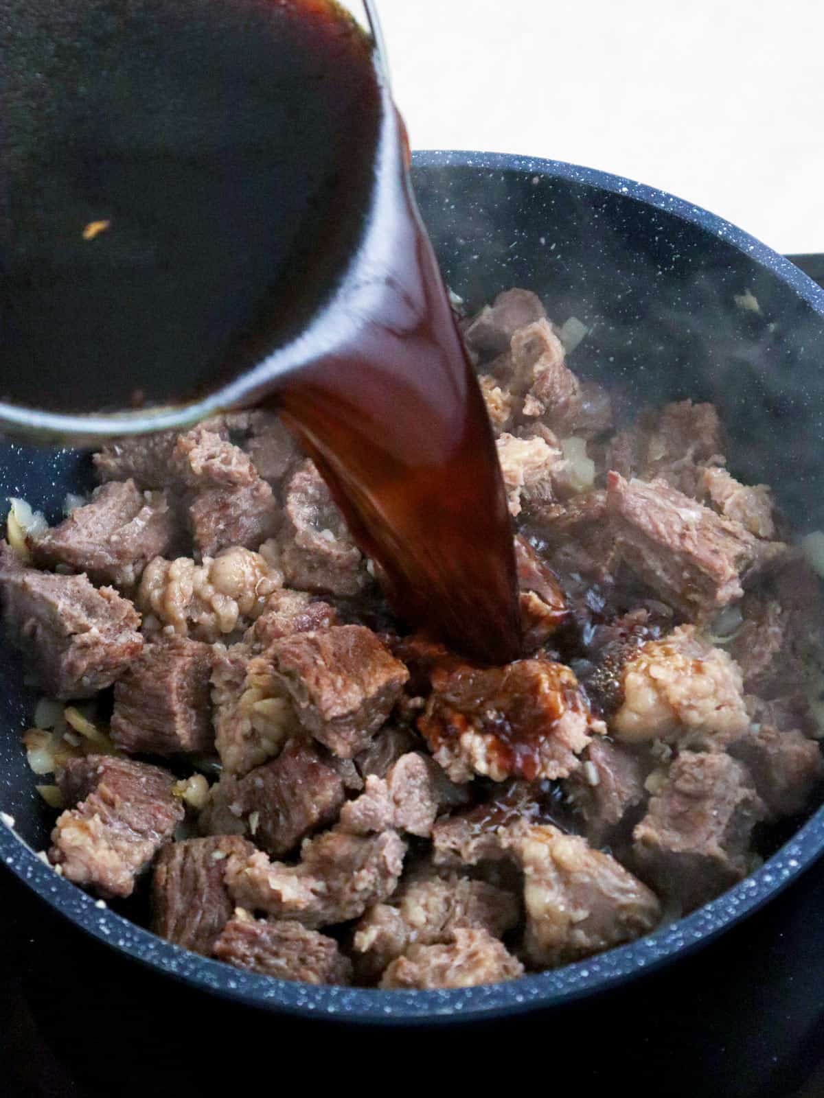 pouring soy sauce over beef in a pot