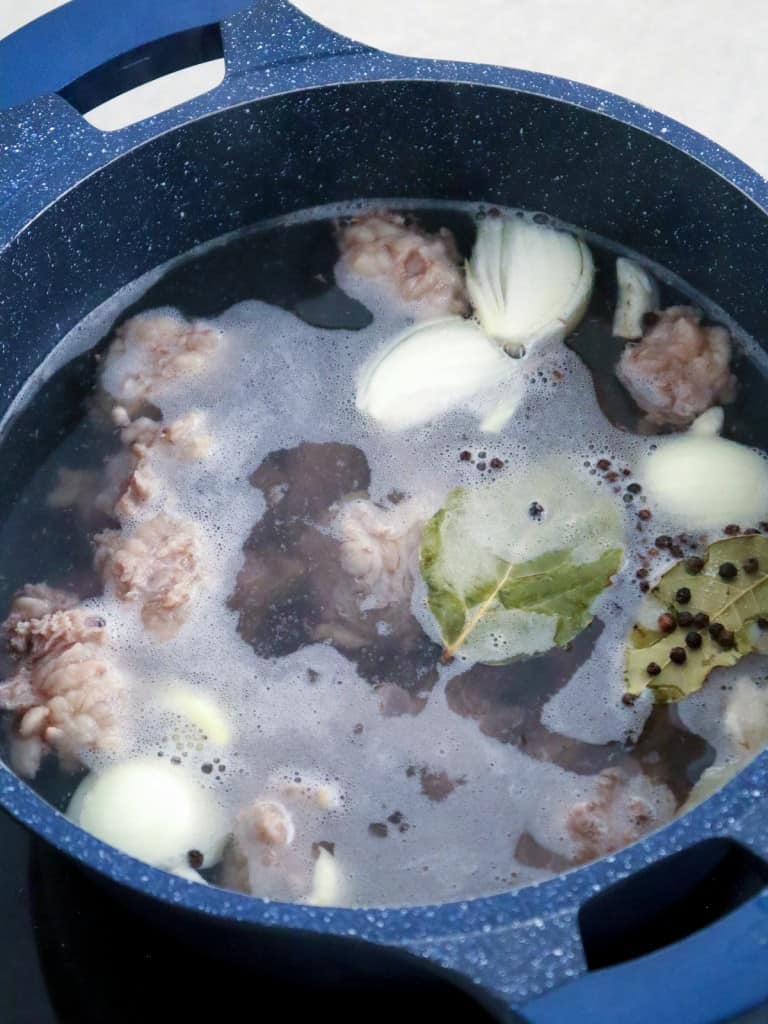 simmering beef cubes in a pot with onions, garlic, peppercorns, and bay leaves