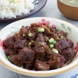 Beef Pares in a serving bowl with a plate of sinangag and broth on the side