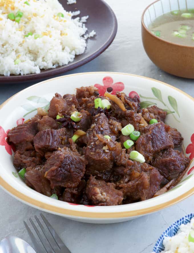 Beef Pares in a serving bowl with a plate of sinangag and broth on the side