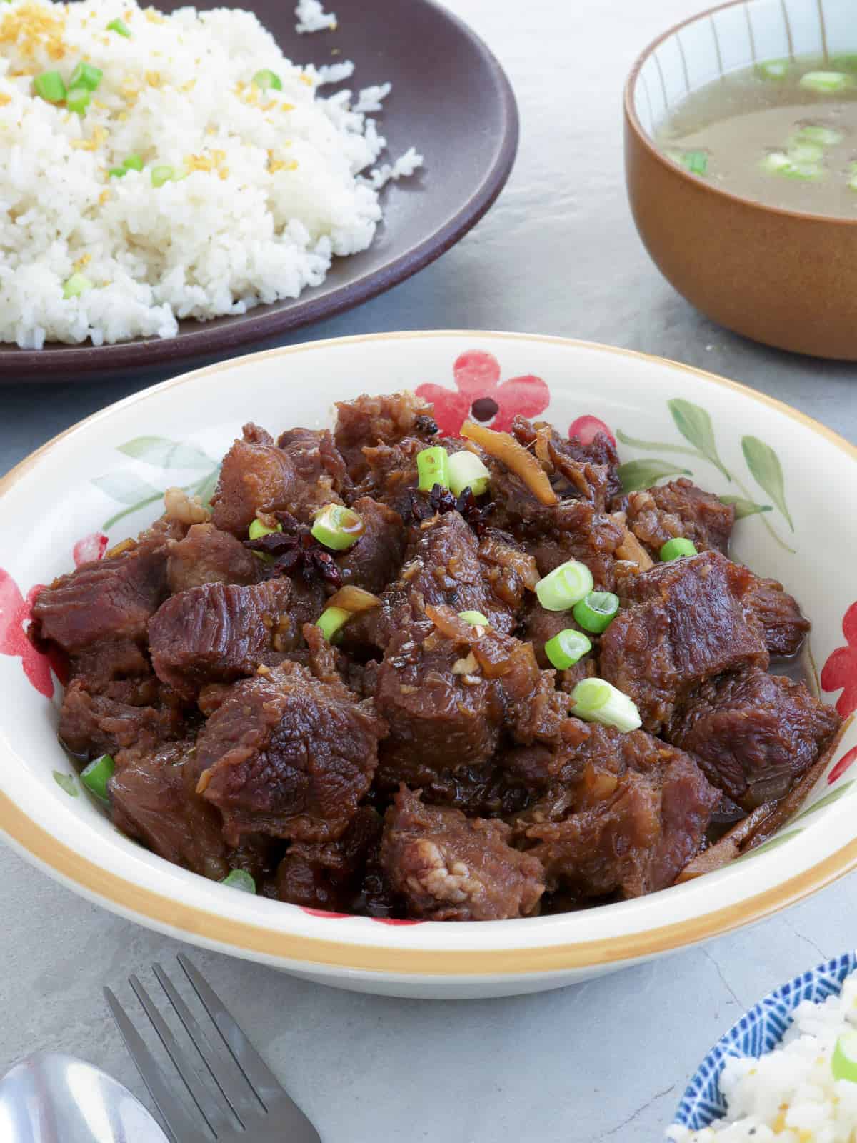 Beef Pares in a serving bowl with a plate of sinangag and broth on the side