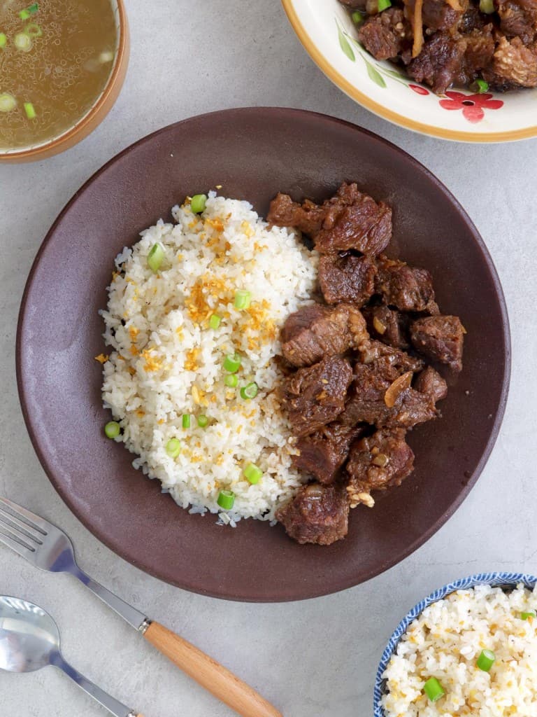 braised beef and garlic fried rice in a brown bowl with a bowl of broth on the side