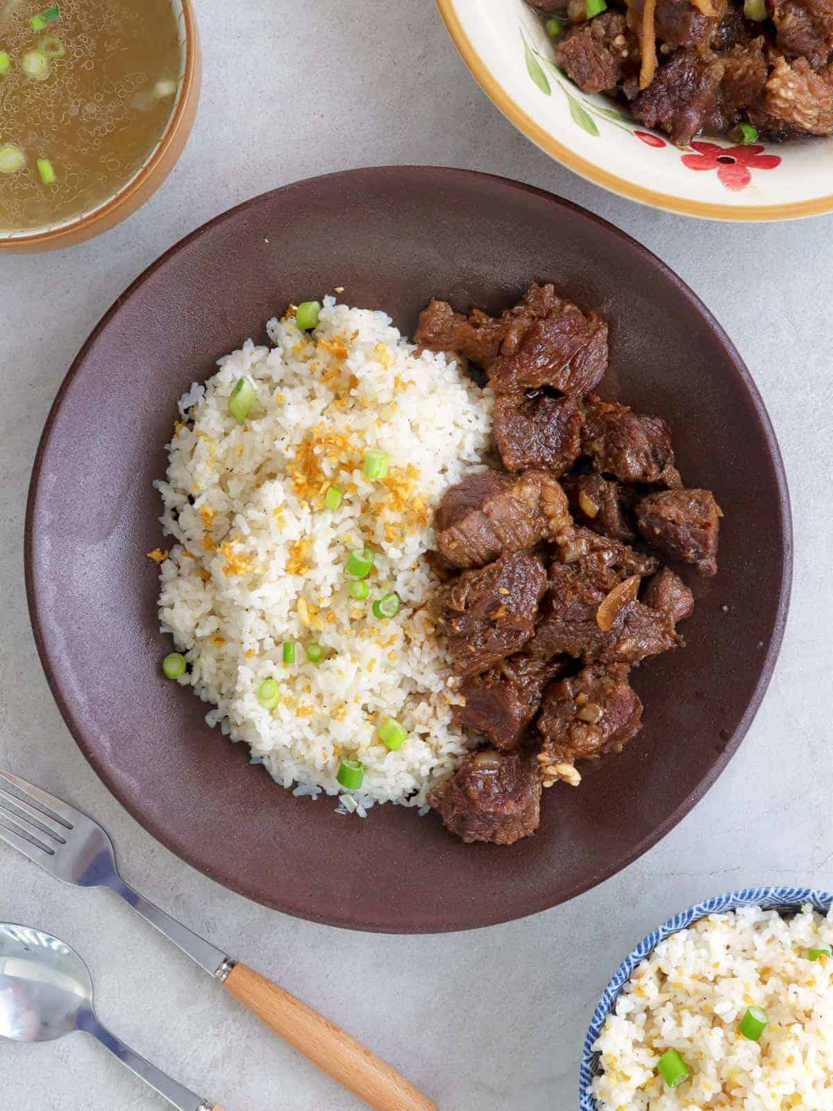 braised beef and garlic fried rice in a brown bowl with a bowl of broth on the side