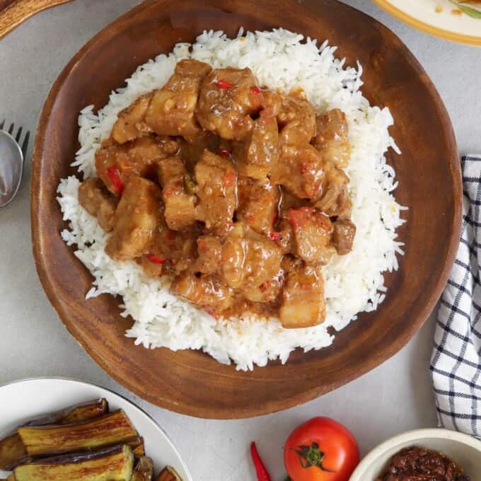 Pork Binagoongan with coconut milk over rice on a wooden plate