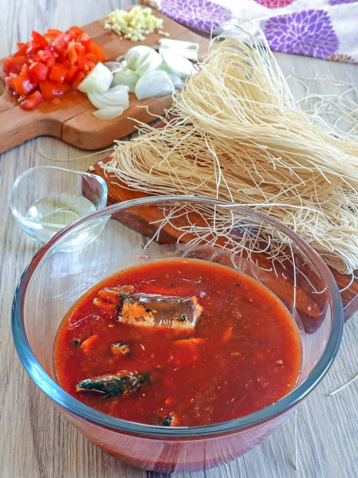 sardines in tomato sauce in a bowl, miswa noodles, chopped onions, garlic, and tomatoes