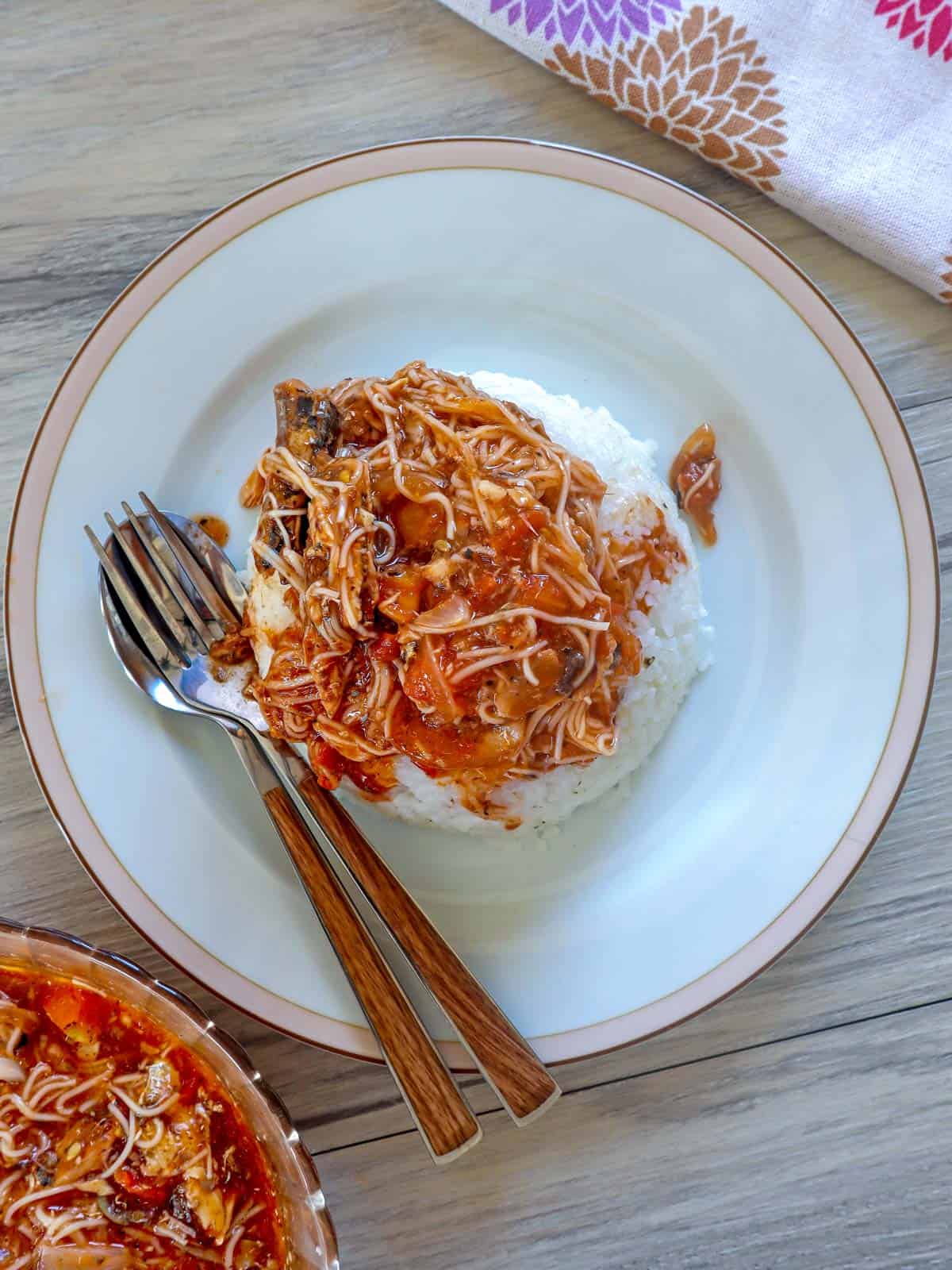 sauteed sardines with misua and tomato sauce over steamed rice on a plate with fork and spoon